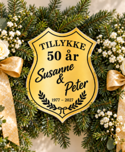 Nærbillede af personligt guldbryllupsskjold blandt gran, hvide blomster og guldbånd på en æresport.